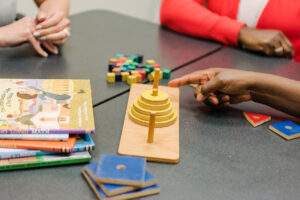 Children's toys and books on a table, with hands pointing to objects